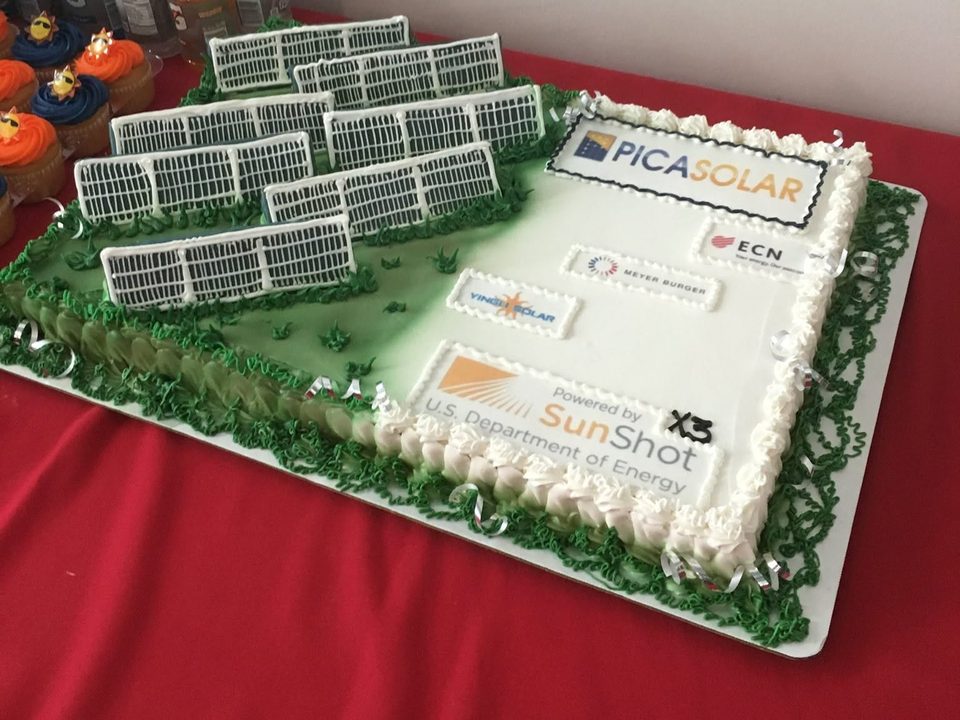 A sheet cake decorated as a solar farm, with rows of icing solar panels, the Picasolar logo, its partners' logos and a SunShot logo marked X3